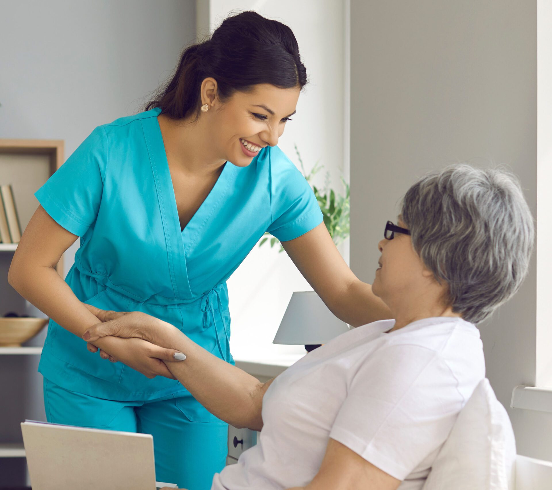 Happy elderly woman patient lying on bed with book talking to caregiver